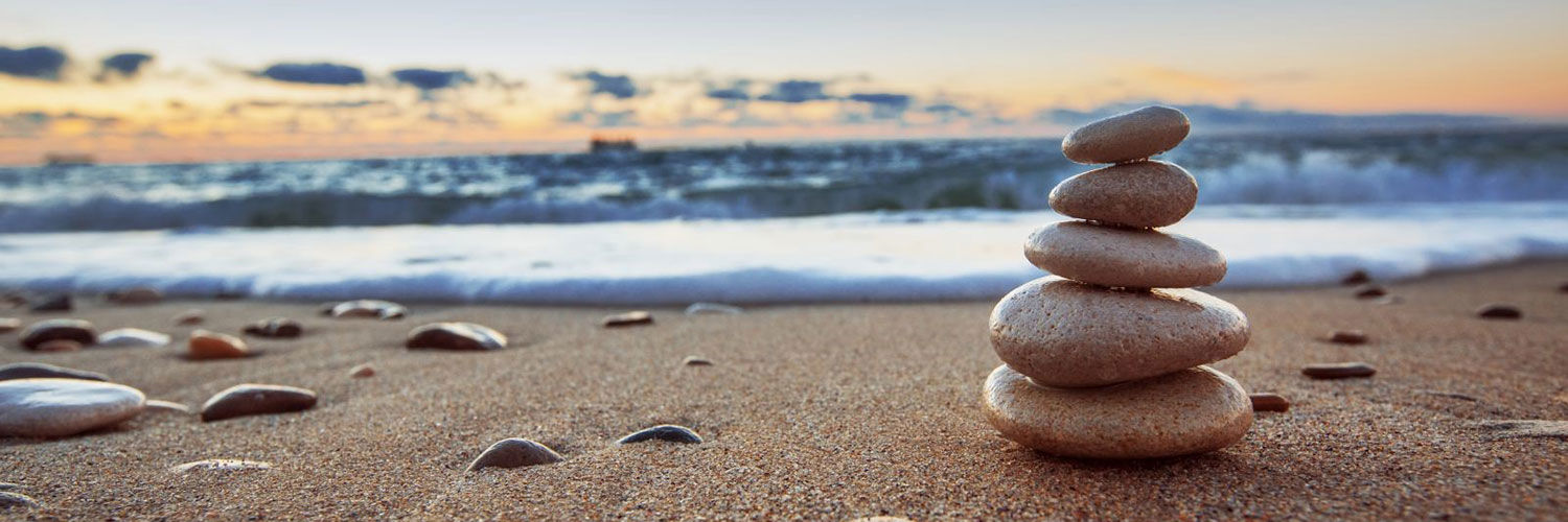 Close up of pebbles stacked up on a beach, with the sea and sky in the background