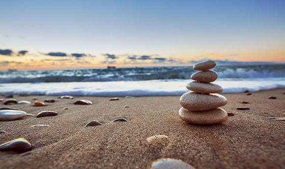 Close up of pebbles stacked up on a beach, with the sea and sky in the background