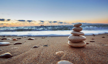 Close up of pebbles stacked up on a beach, with the sea and sky in the background