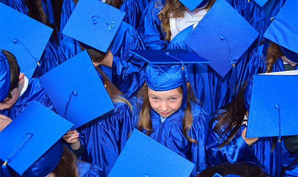 A group of young children in blue graduation caps and gowns, one is smiling up at the camera