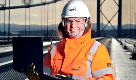 A young engineer on the Forth Road Bridge wearing PPE and holding a laptop