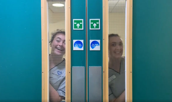 Two QMU Nursing Students peeking through a door window