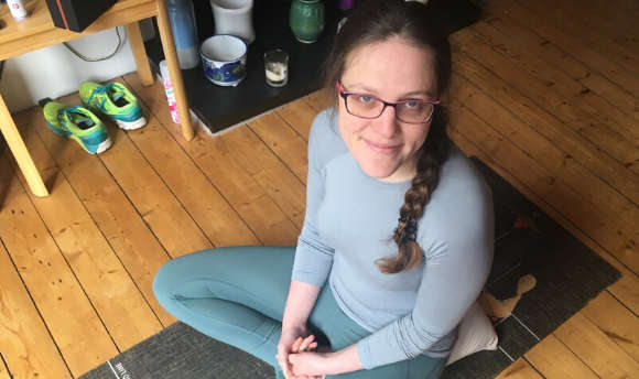 Kate brown sitting cross legged on a yoga matt at home
