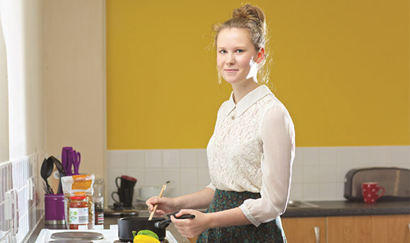 Portrait of a young woman cooking something on a a stovetop cooker