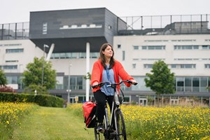A young woman cycling through a field of yellow flowers on Queen Margaret University campus