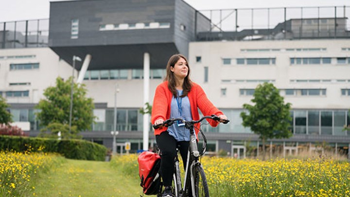A young woman cycling through the field outside the Queen Margaret University campus