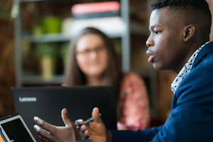 A Queen Margaret University student sitting at a laptop and talking confidently to a small group of people