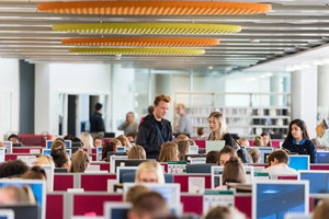 Two Queen Margaret University students standing in a busy library, deep in conversation