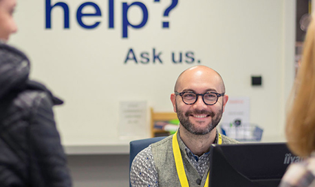 QMU Librarian at his desk smiling and chatting with two women 