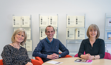Three well dressed adults round a table smiling at the camera