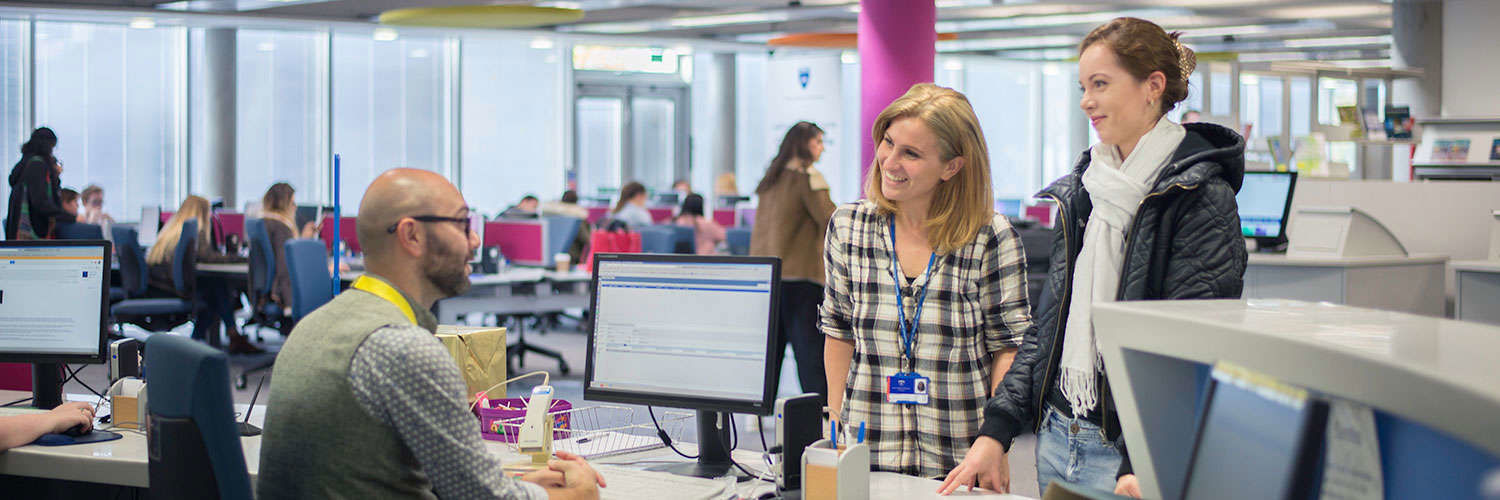 QMU Librarian at his desk smiling and chatting with two women 
