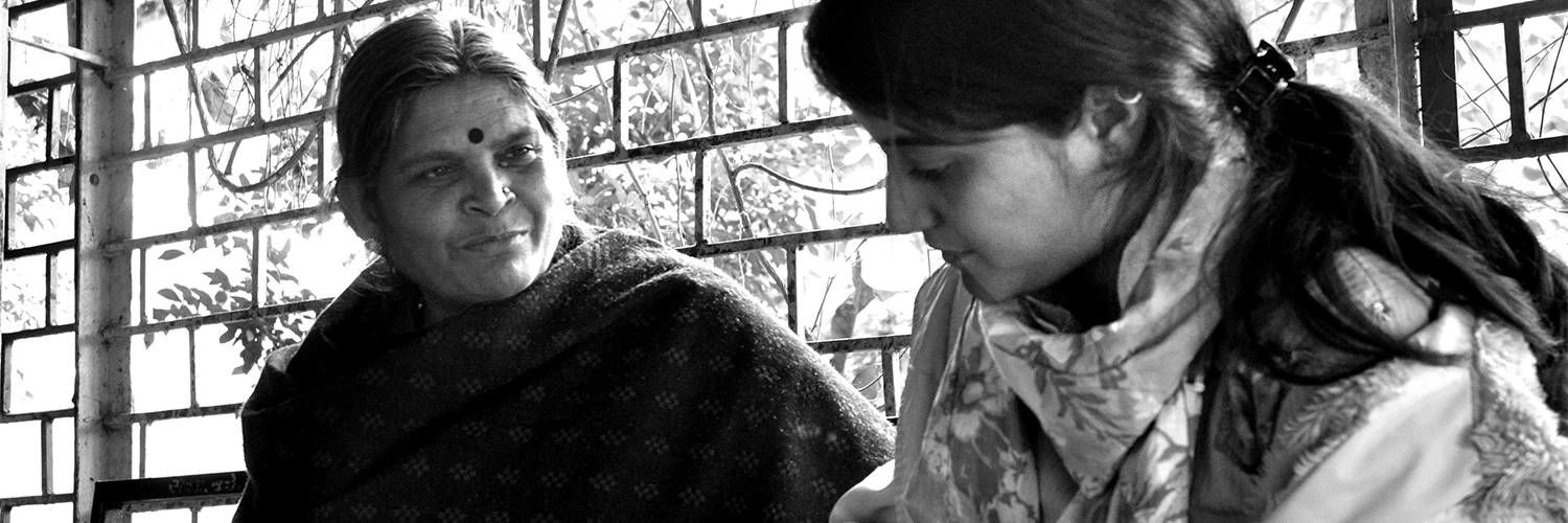 Black and white photograph of a Hindu woman talking to a younger woman taking notes