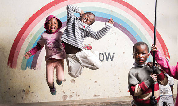 Smiling children jumping off the ground in front of a rainbow painted on the wall