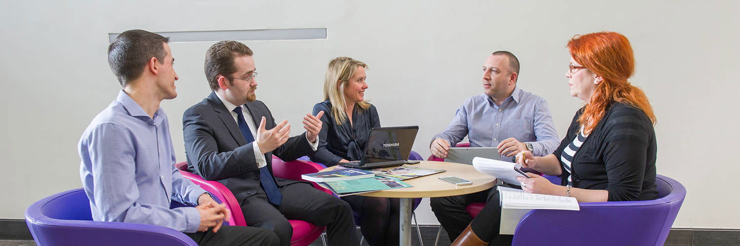 A committee meeting of 5 people taking place round a small table