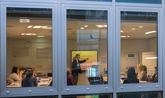 A class being taught photographed from outside through a wall of windows, QMU