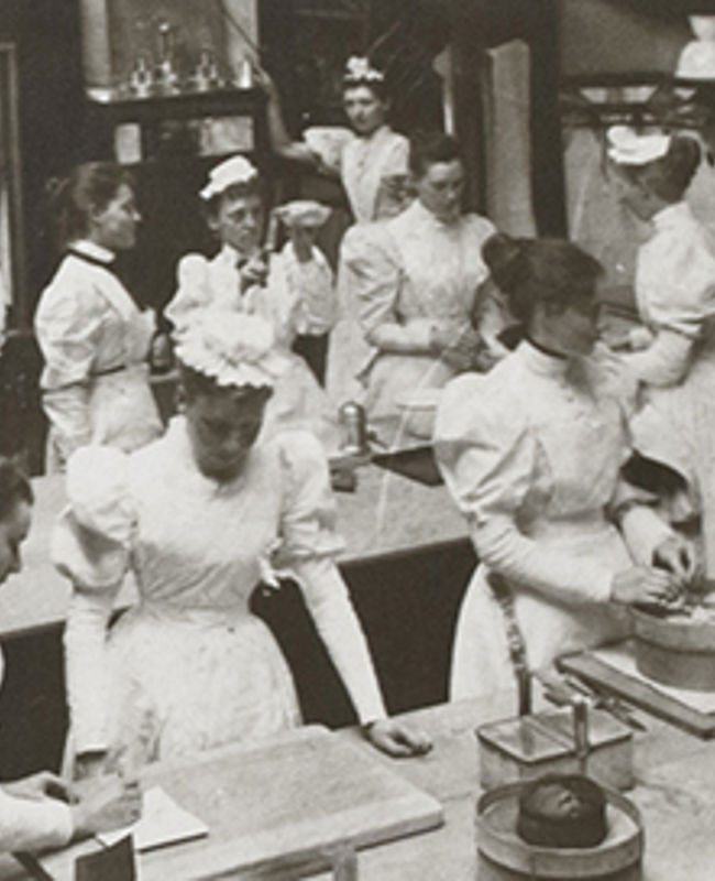 B+W photo of a kitchen full of women in Edwardian style chef's whites
