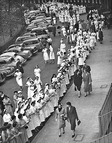 B+W photo of hundreds of women in white dresses lined up along a pavement edge