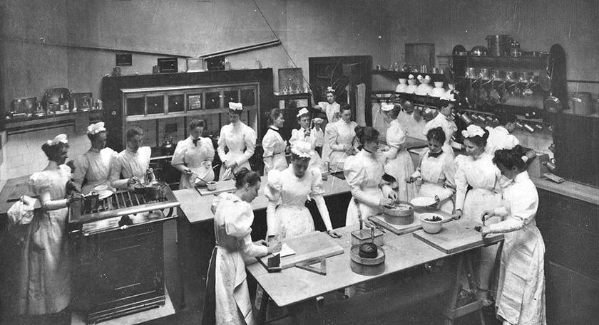 B+W photo of a kitchen full of women in Edwardian style chef's whites