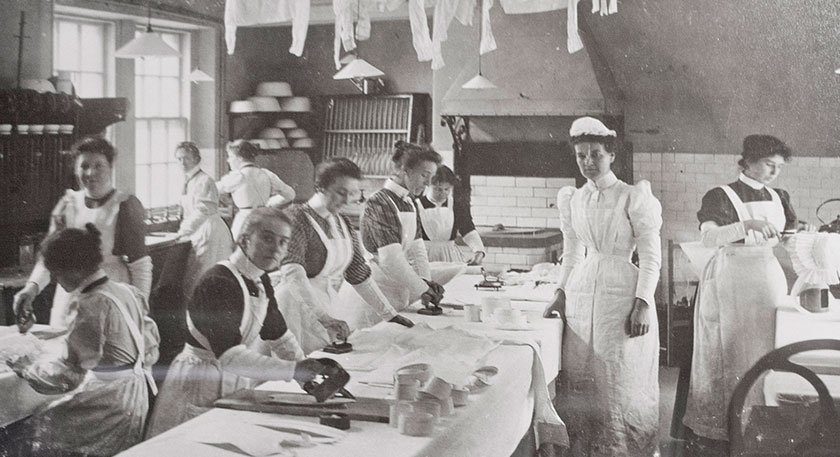 B+W photo of a kitchen full of women in Edwardian style chef's whites