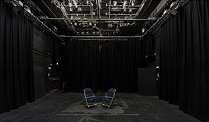 Empty performance room with two single folding chairs set up centre stage