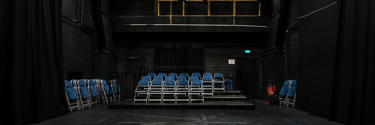 Empty performance room with folding chairs set up on the risers and a large light rig