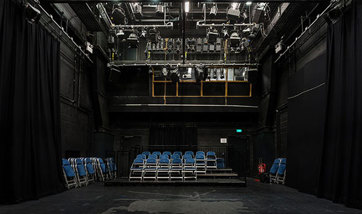 Empty performance room with folding chairs set up on the risers and a large light rig