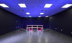 A dimly lit performance studio with two empty chairs centre stage, QMU