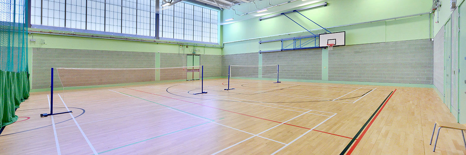 A large, bright sports hall with tennis nets, basketball nets and large windows