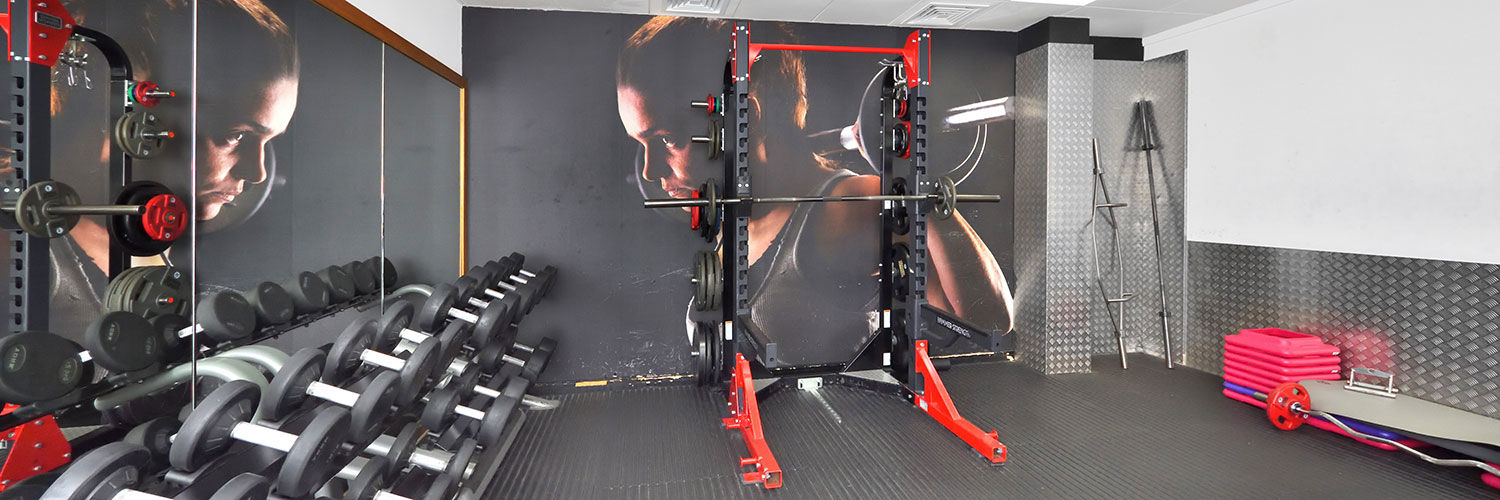 A bright, modern weights room in the gym with a large variation in weights & a squat rack