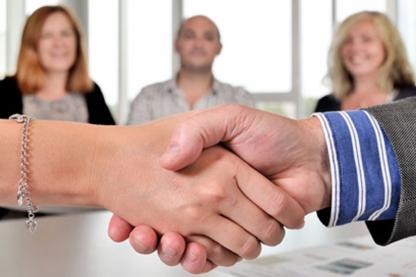 Close up of a pair of shaking hands, 3 people smile on in the background
