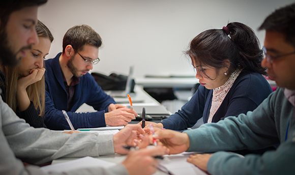 A group of QMU students writing in their notepads at a table together