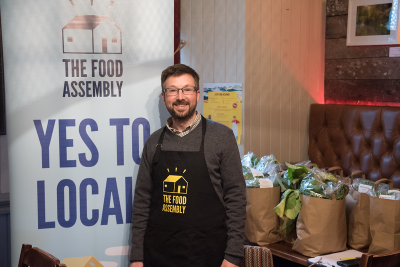 A QMU Student wearing a Food Assembly apron surrounded by bags of fresh produce