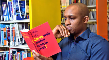 A young man sitting in the library, intently reading a book about financial crisis avoidance