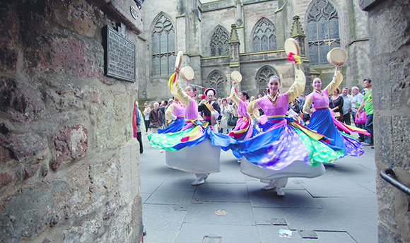 A group of dancers in brightly coloured dresses performing on the streets of Edinburgh