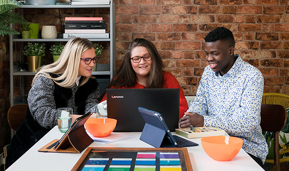 A group of QMU students laughing at a table together, working on laptops and ipads