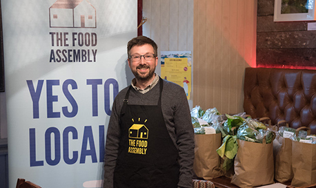 A QMU Student wearing a Food Assembly apron surrounded by bags of fresh produce