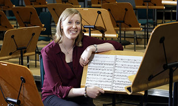 A young woman leaning on a sheet music stand and smiling at the camera 