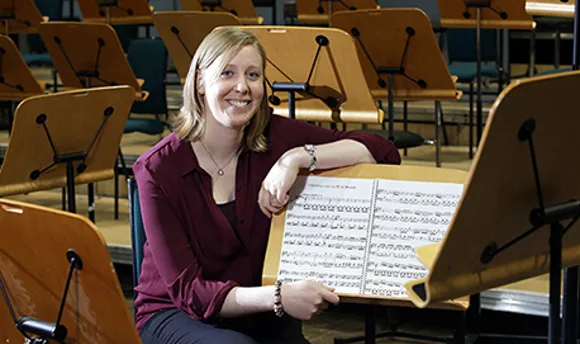 A young woman leaning on a sheet music stand and smiling at the camera