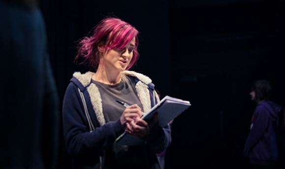 A QMU stage management student reading and making notes on a notepad on stage