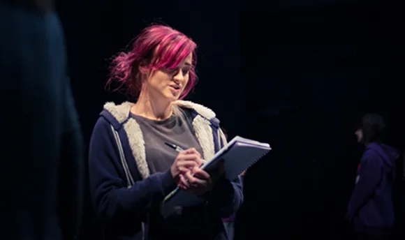 A QMU stage management student reading and making notes on a notepad on stage