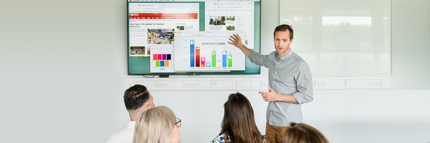 A lecturer giving a presentation on user statistics to a digital communications class 