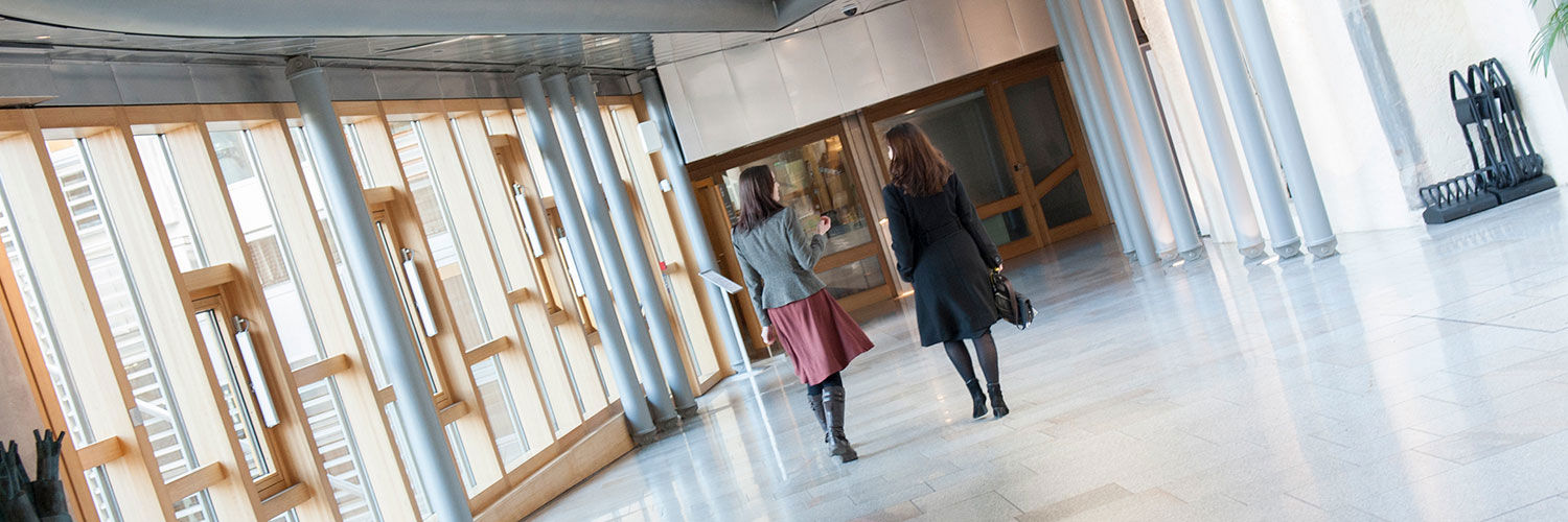 Two women walking down a corridor in Queen Margaret University hallway