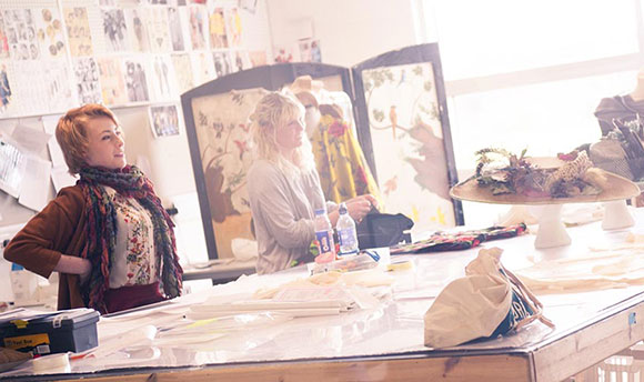 Queen Margaret University Costume Design students standing by a table surrounded by designs, materials and costumes