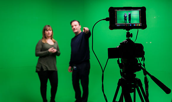 A Queen Margaret University student being briefed in front of a green screen