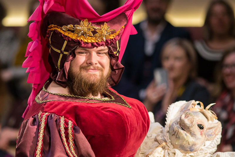 A bearded model wearing a red medieval velvet dress and headpiece