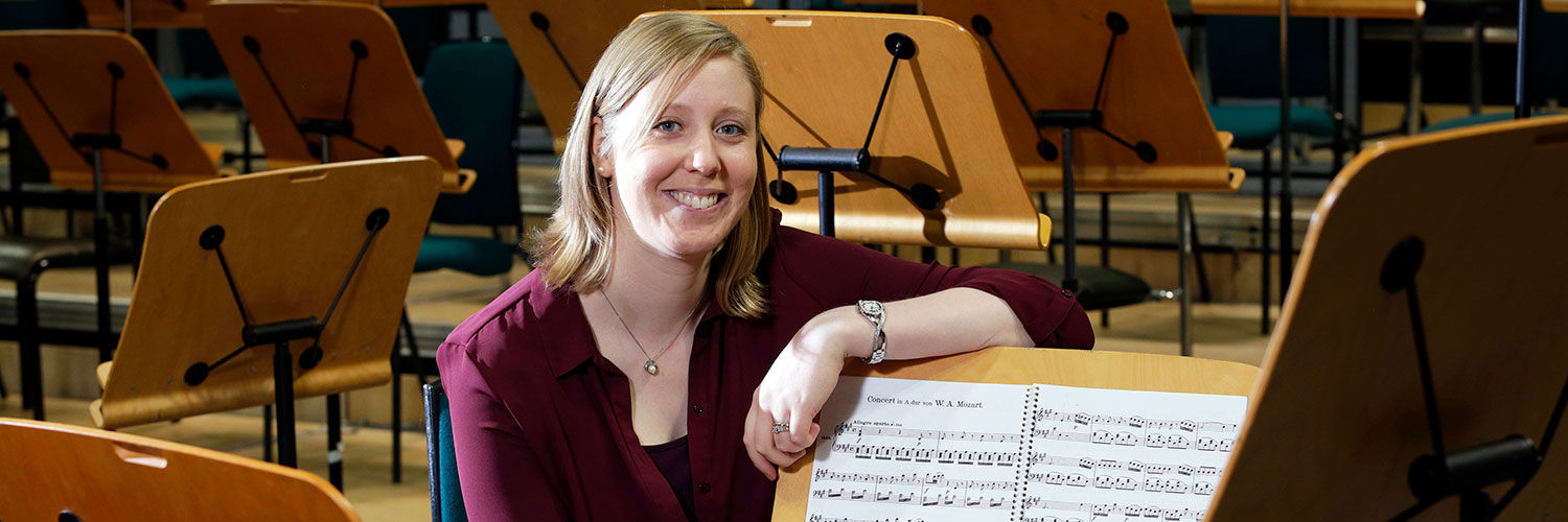 A young woman leaning on a sheet music stand and smiling at the camera