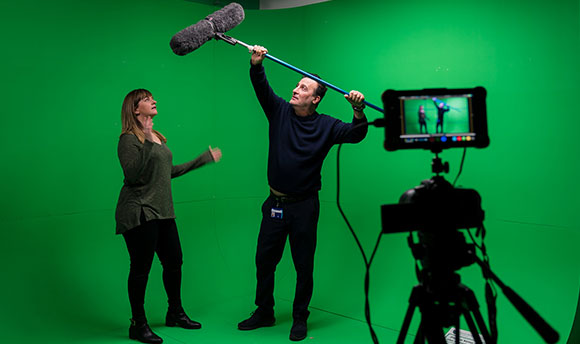 Students filming using a green screen, using a professional camera + boom mic