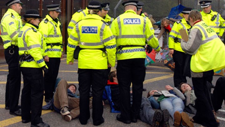 Police members surrounding a group of individuals lying on the street