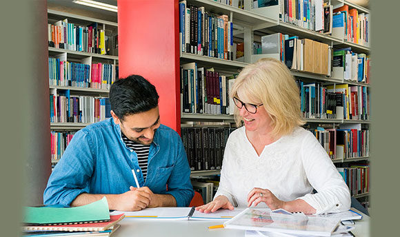 A woman and student sat at a table together reading through a book and smiling