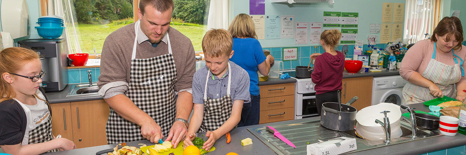 Home Economics teacher and pupils wearing aprons and chopping fruit in kitchen